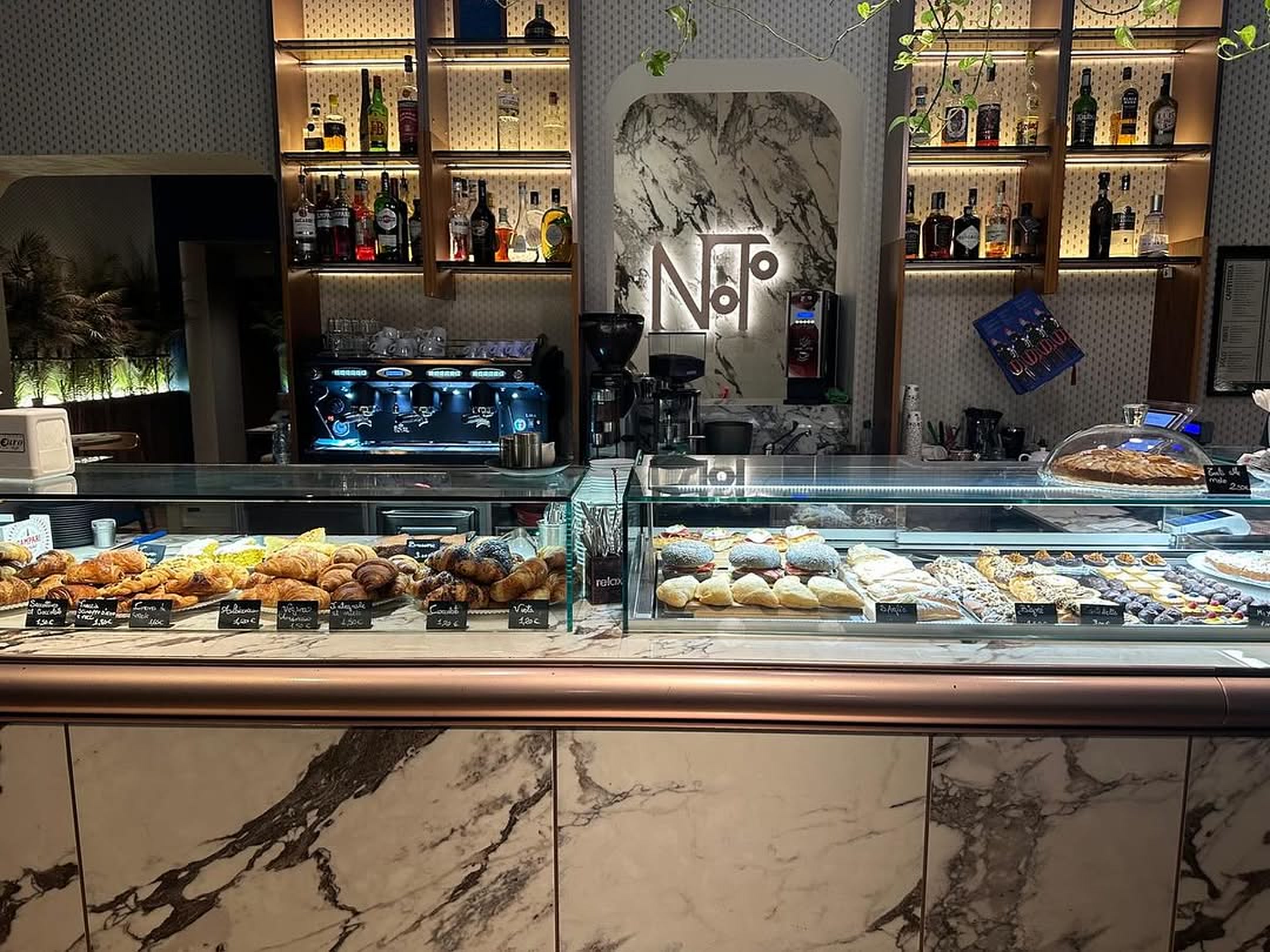 Il banco di Noto: la vetrina dei dolci, la macchina del caffè e l'insegna illuminata sotto l'arco di marmo