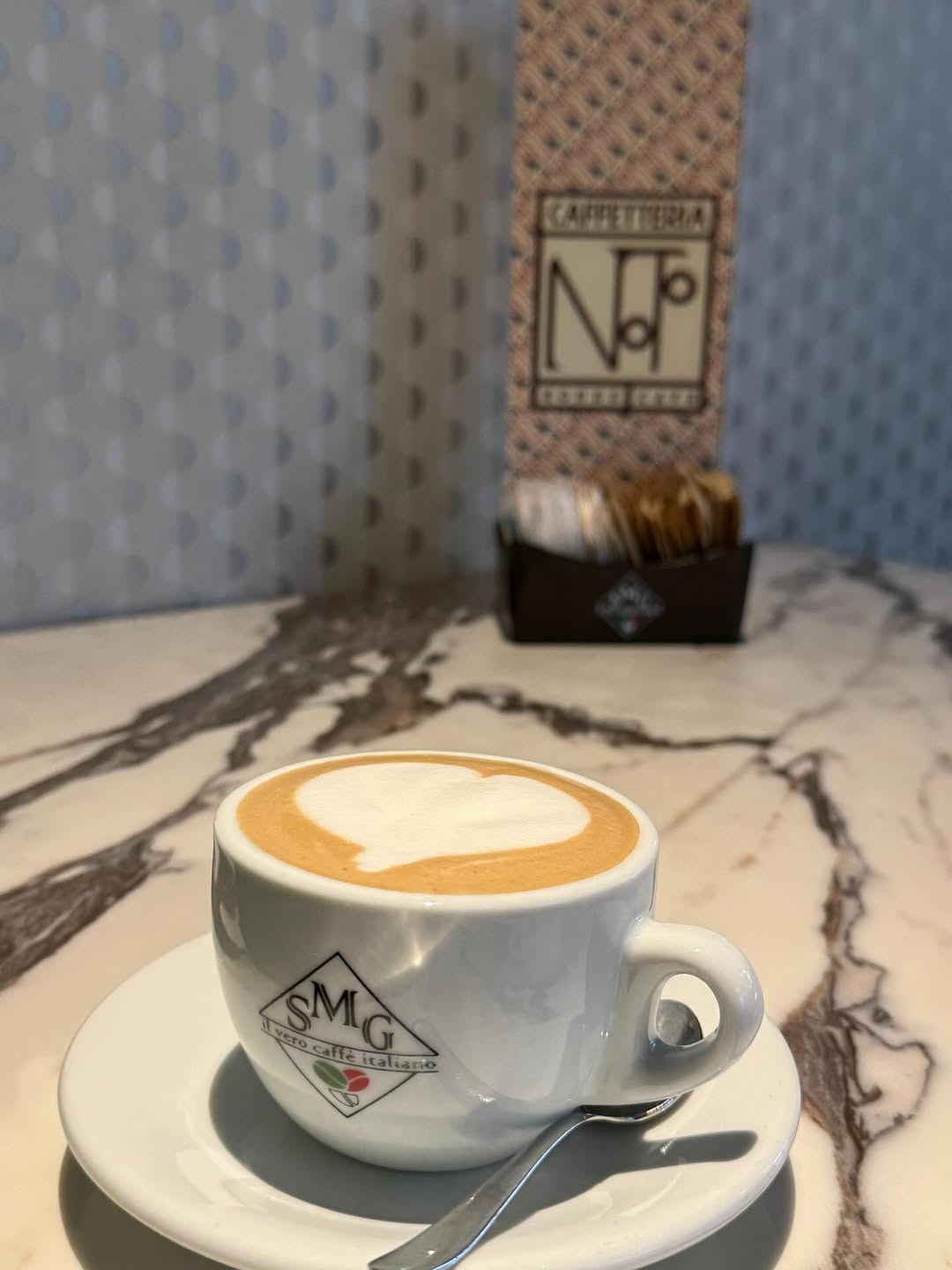 Cappuccino con cuore di latte sul tavolo in marmo, con l'insegna Caffetteria Noto
